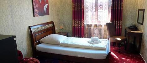 A hotel room with a bed, a chair, a desk, and a window with curtains.