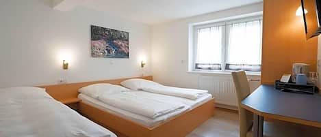 Habitación de hotel con dos camas, un escritorio, una silla, un radiador y una ventana con cortinas.