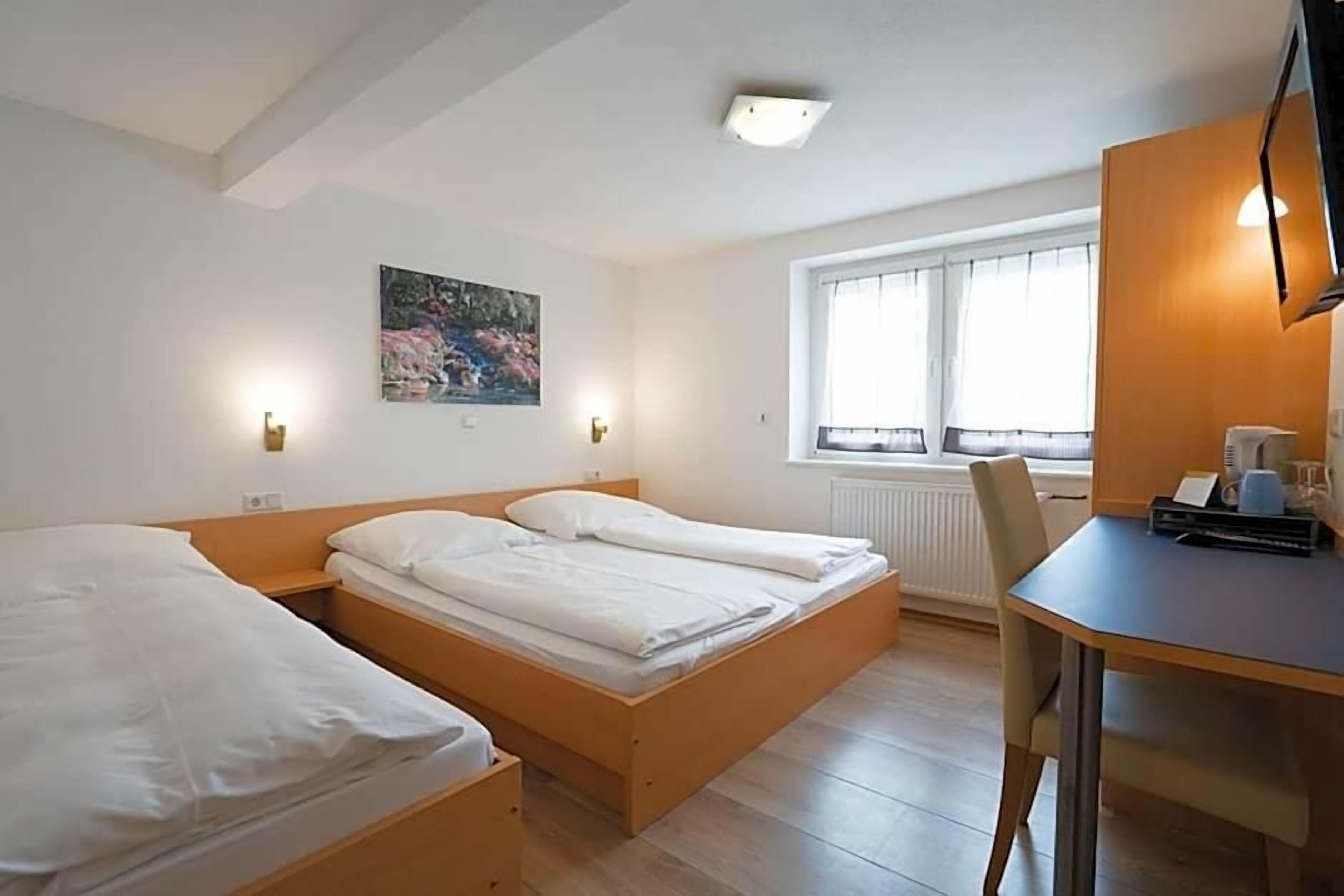 Habitación de hotel con dos camas, un escritorio, una silla, un radiador y una ventana con cortinas.