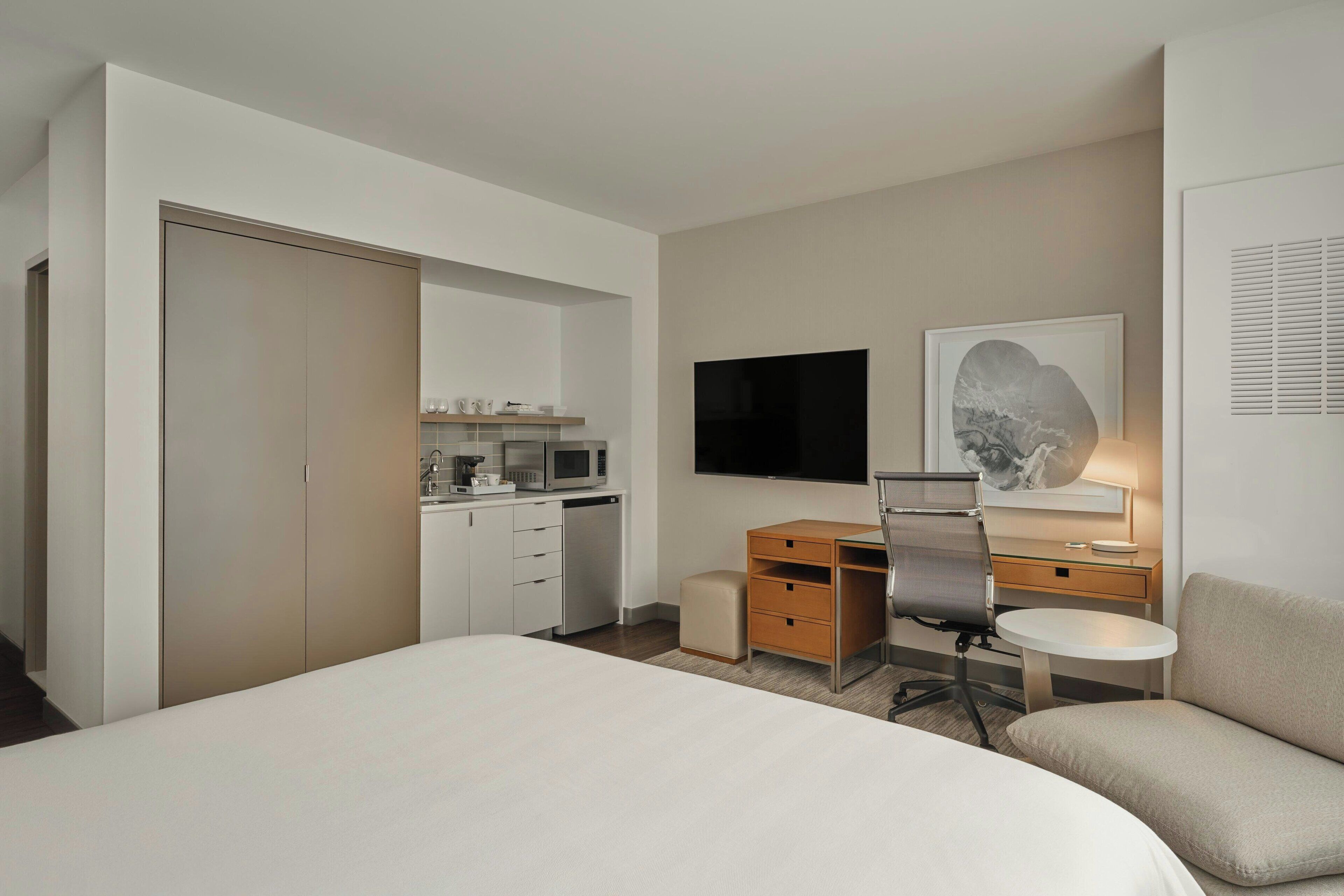 A hotel room with a bed, a desk with a chair, a television, a small table, and a sofa.
