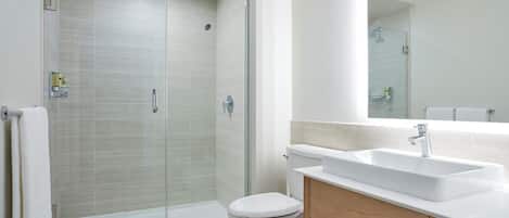 A modern bathroom with a glass shower enclosure, a white toilet, and a wooden vanity with a sink.