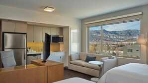 A modern hotel room with a kitchenette, a sofa, a bed, and a large window offering a city and mountain view. - Element by Marriott Basalt - Aspen (Basalt)