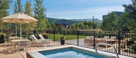 Una piscina con una escalera de metal, rodeada de sillones de descanso y una mesa con sombrilla.