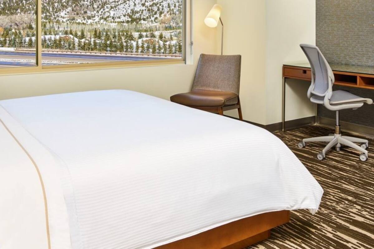 A hotel room with a large bed, a desk, a chair, a TV, and a view of a snowy landscape.