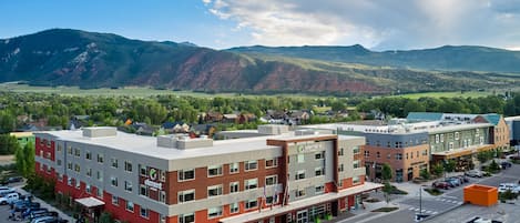 A multi-story hotel with a red and grey facade, located in a town with a mountainous backdrop.