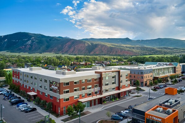 A multi-story hotel with a red and grey facade, located in a town with a mountainous backdrop.