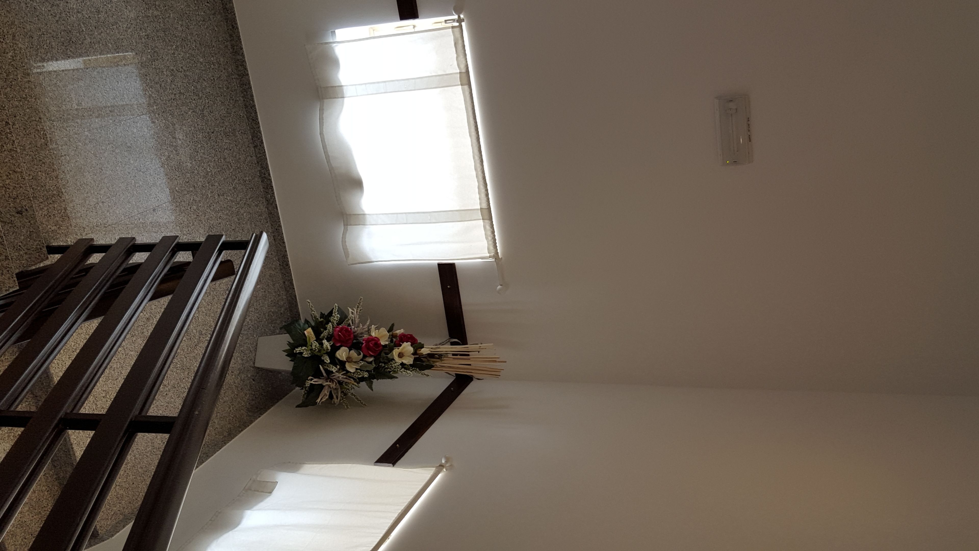 A room with a wooden bench, a window with blinds, and a bouquet of flowers on a table.