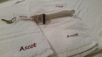 En stak hvide håndklæder med broderet tekst "Ascot" og et skilt med teksten "HOTEL ASCOT CAIANELLO 23".