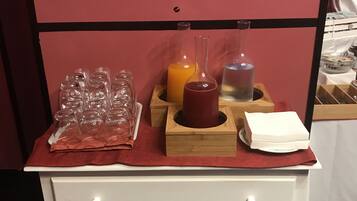 Eine weiße Kommode mit Schubladen, eine rote Unterlage sowie verschiedene Gegenstände, darunter ein Glasbehälter, eine Orangensaftflasche, ein Glas Wasser und ein Servietttuch.