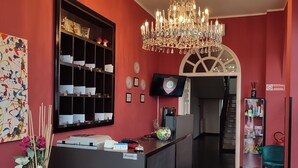 A reception area with a chandelier, a reception desk, a wall-mounted TV, and a flower arrangement. - Ascot Hotel (Caianello)