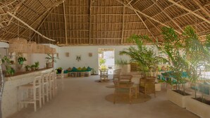 A spacious room with a high thatched ceiling, wicker furniture, and potted plants. - Cristal Resort (Paje)