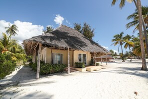 A beach house with a thatched roof, surrounded by palm trees and a sandy beach.