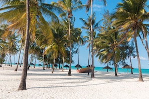 A beach with palm trees, a boat, and thatched umbrellas. - Cristal Resort (Paje)