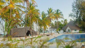 A resort with a pool, palm trees, and thatched-roof huts. - Cristal Resort (Paje)