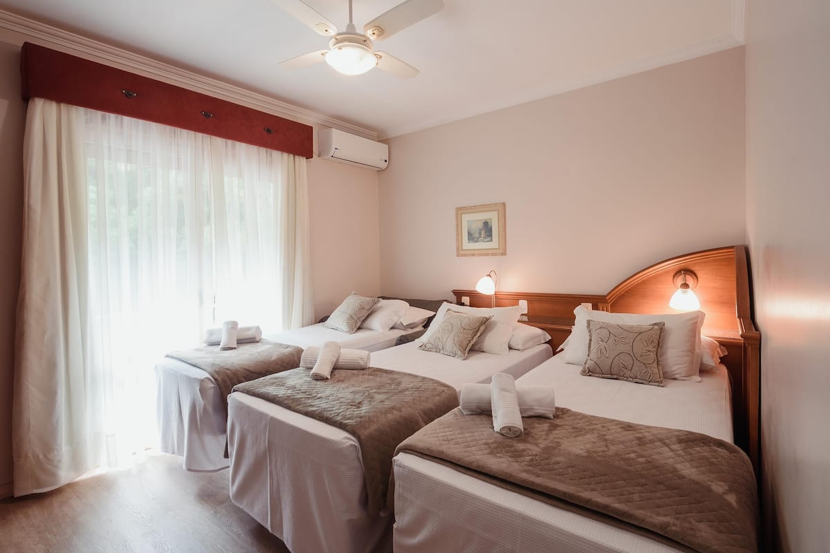 A hotel room with two beds, a ceiling fan, an air conditioning unit, a bedside lamp, and a framed picture on the wall.