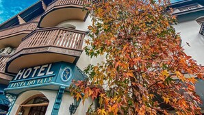 Un hotel con un balcón y un árbol con hojas otoñales al frente.
