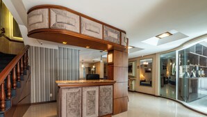 A modern hotel lobby with a curved reception desk, a staircase with wooden balusters, and a glass partition with decorative items. - Hotel Vista do Vale (Gramado)