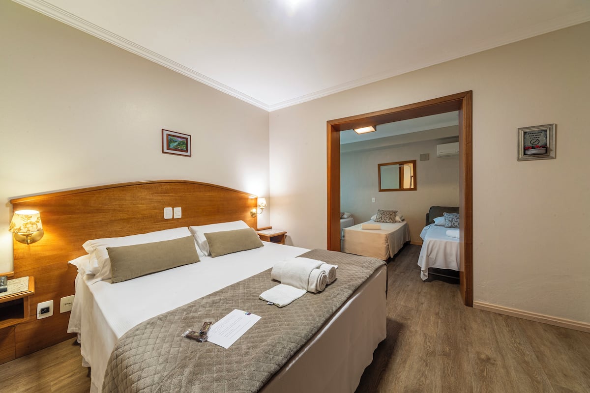 A hotel room with a large bed, bedside tables, a mirror, and a door leading to another room.
