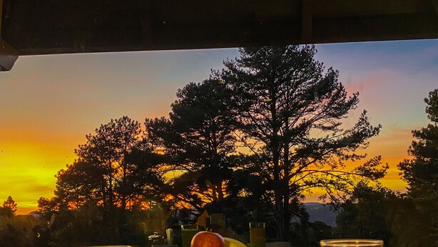 Una mesa con vista al atardecer, con un plato de sandía y otras frutas, y dos vasos de jugo.