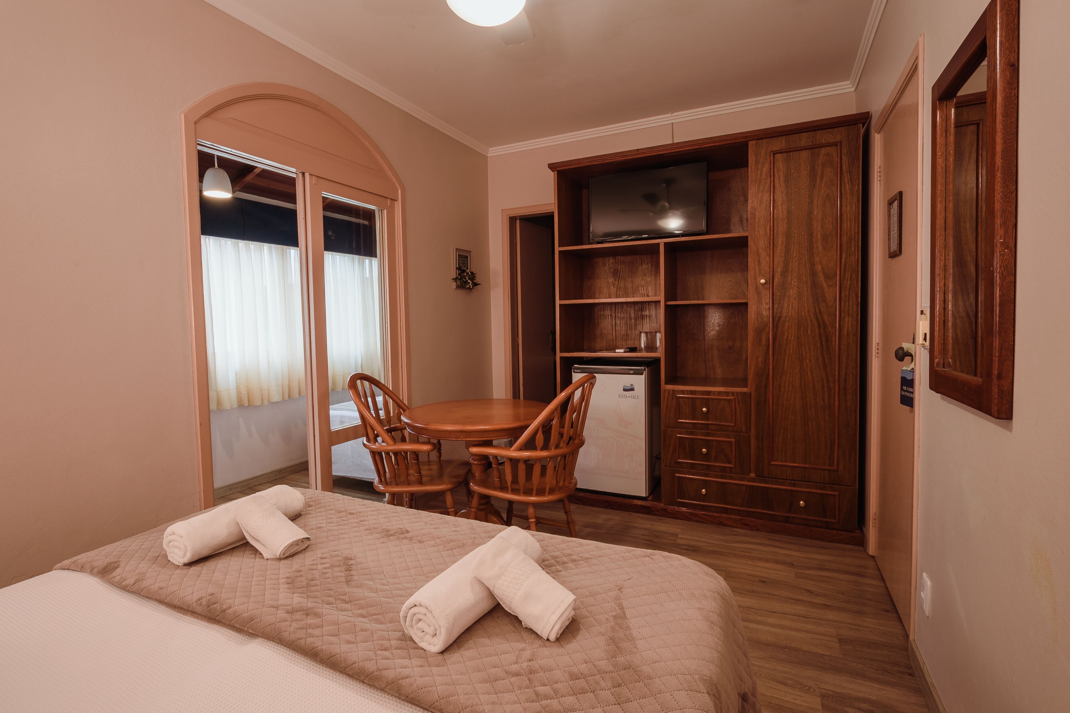 A hotel room with a bed, a desk, a chair, a television, and a wardrobe.