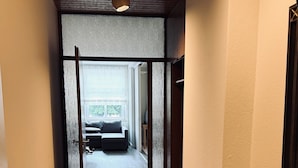 A hallway with wooden flooring, a bench, and a view into a room with a bed and window. - Hotel Wissers by ANS (Fehmarn)