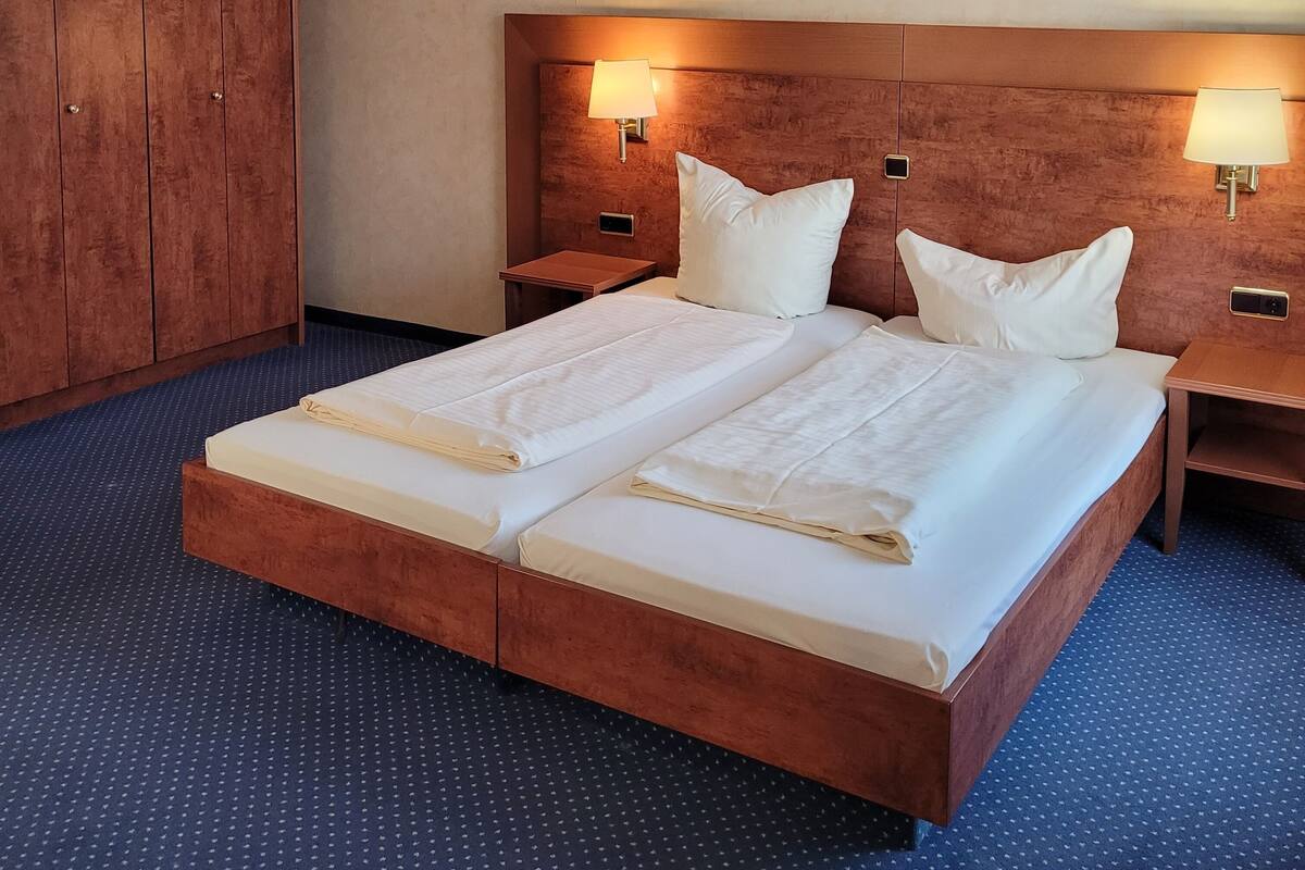 A double bed with two pillows, wooden headboard, two bedside tables with lamps, and a wardrobe.