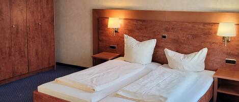 Una cama doble con dos almohadas, cabecera de madera, dos mesitas de noche con lámparas y un armario.