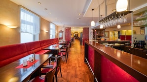 A restaurant with wooden flooring, red upholstered booths, and a bar area with wine bottles and glasses. - Hotel Wissers by ANS (Fehmarn)