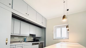 A modern kitchen with white cabinets, a large island, and a window providing natural light. - Hotel Wissers by ANS (Fehmarn)
