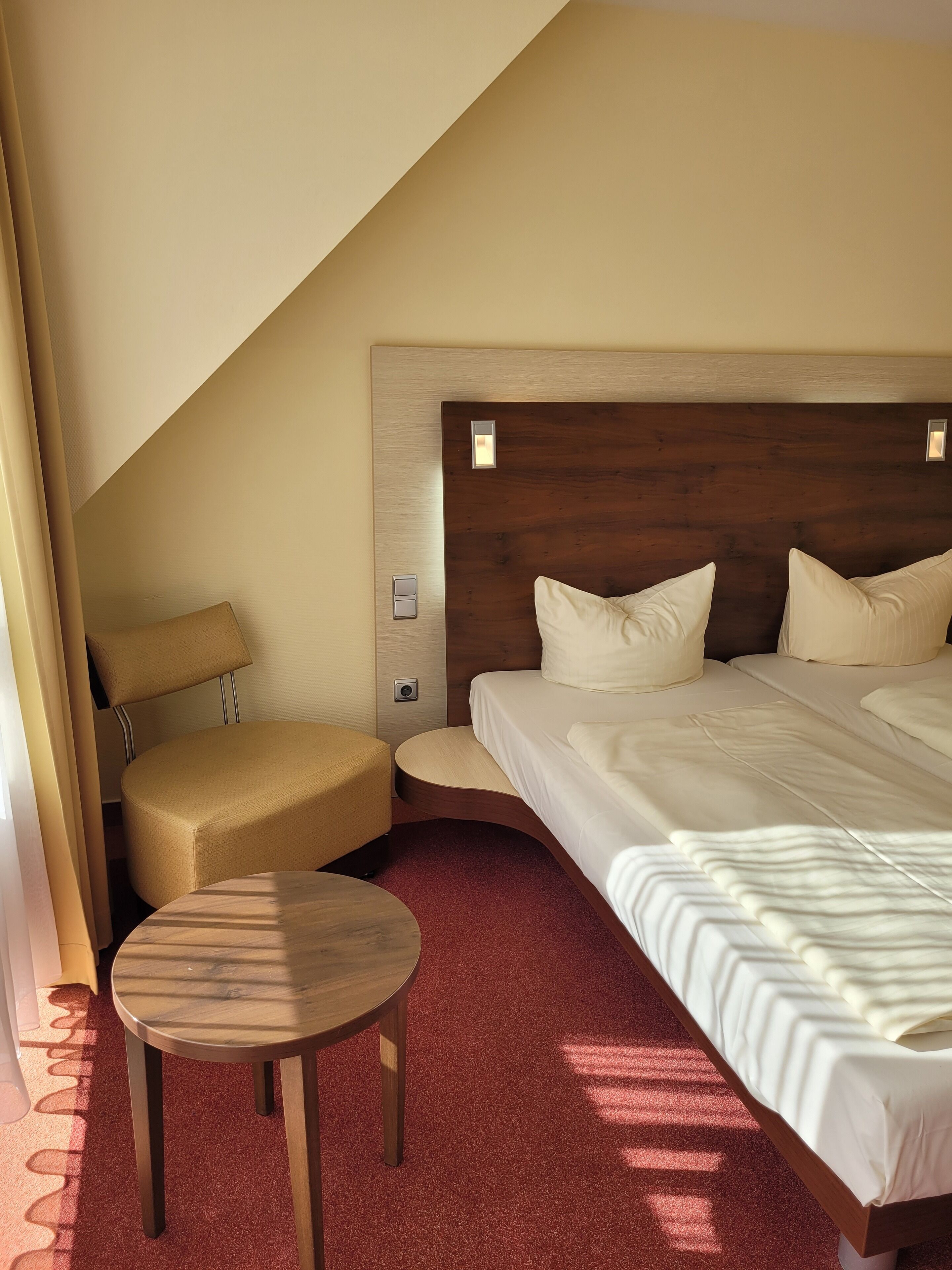 A hotel room with a large bed, a small round table, a chair, and a wooden headboard.