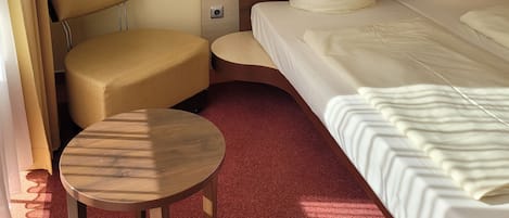 A hotel room with a large bed, a small round table, a chair, and a wooden headboard.