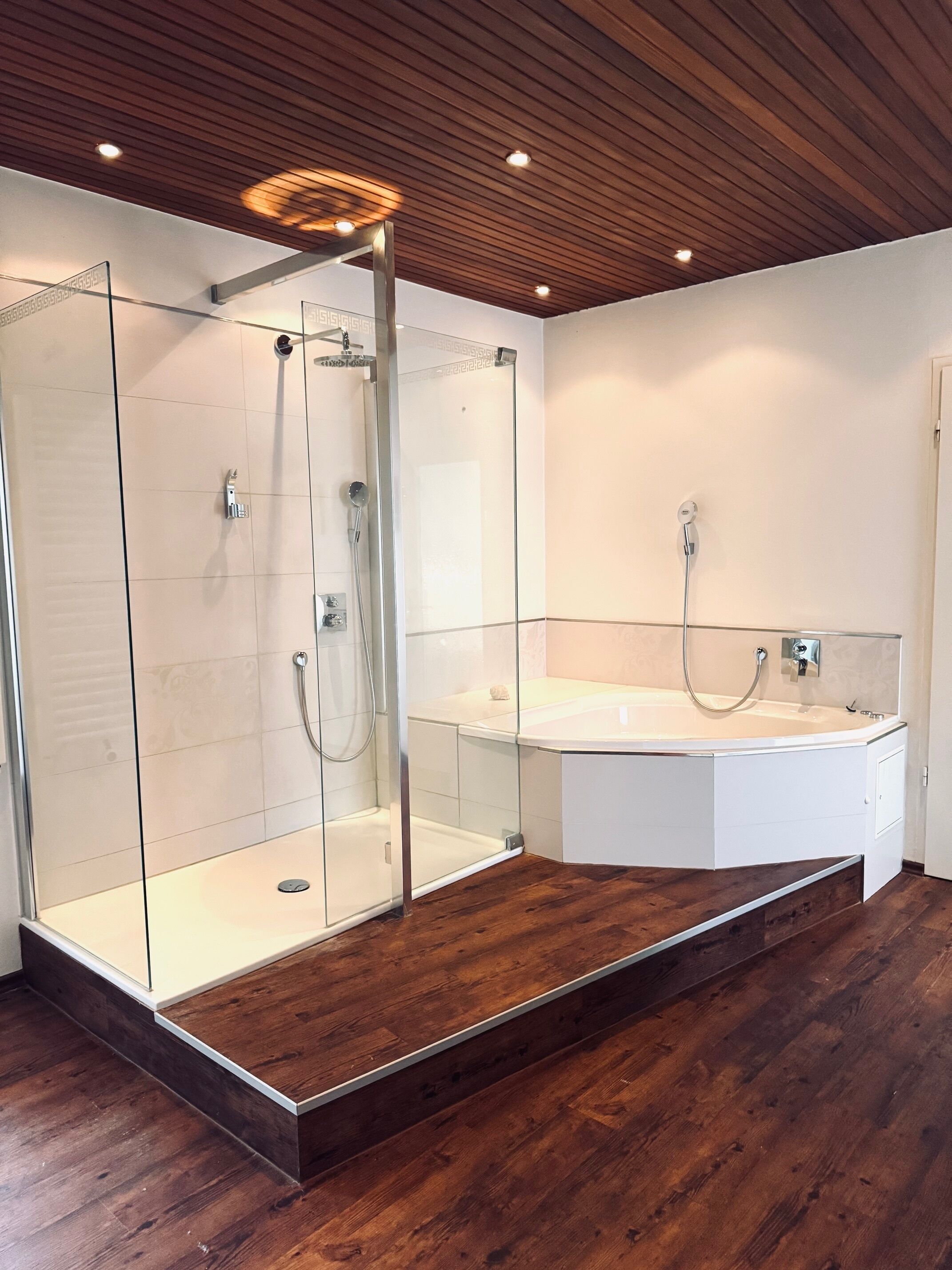 A modern bathroom with a glass-enclosed shower, a freestanding bathtub, and wooden flooring.