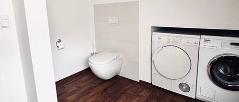 A compact laundry room with a washing machine and dryer, a toilet, and a framed picture on the wall.