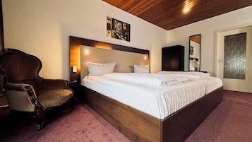 A hotel room with a large bed, a wooden headboard, a chair, and a painting on the wall.