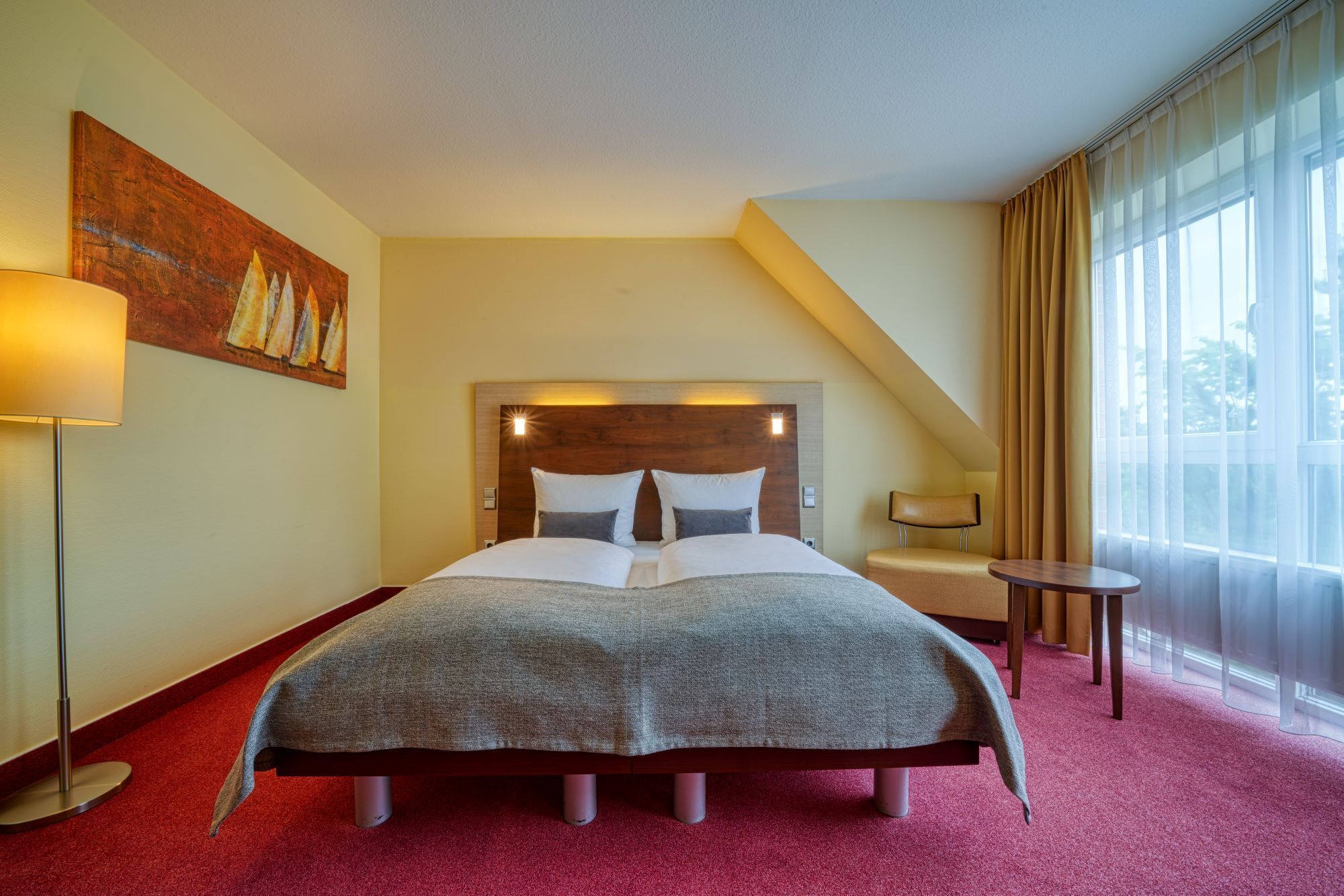 Una habitación de hotel con una cama grande, una mesita de noche, una lámpara y un cuadro en la pared.
