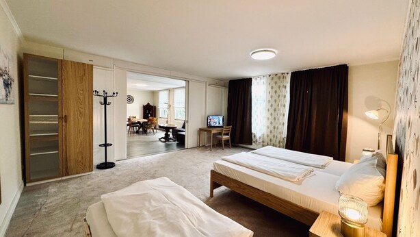 A hotel room with two beds, a desk, a TV, and a dining area visible through an open door. - Hotel Wissers by ANS (Fehmarn)