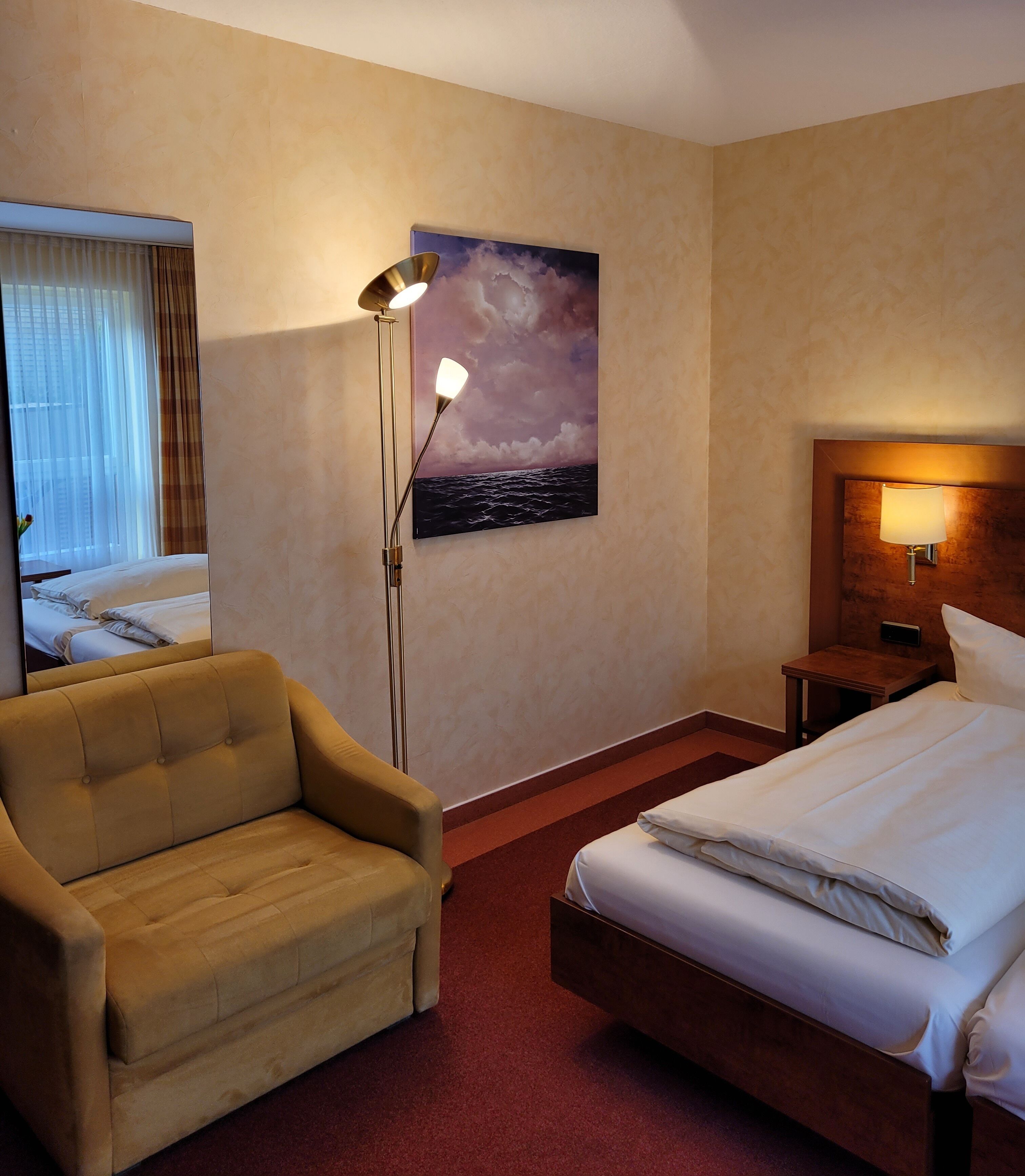 Ett hotellrum med en säng, en soffa, ett nattduksbord, en lampa, en tavla och ett fönster med gardiner.