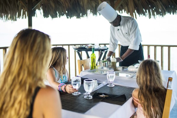 A dining table with a chef preparing food, surrounded by guests.