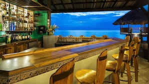 Un bar con vista al océano, muebles de madera y una variedad de botellas.