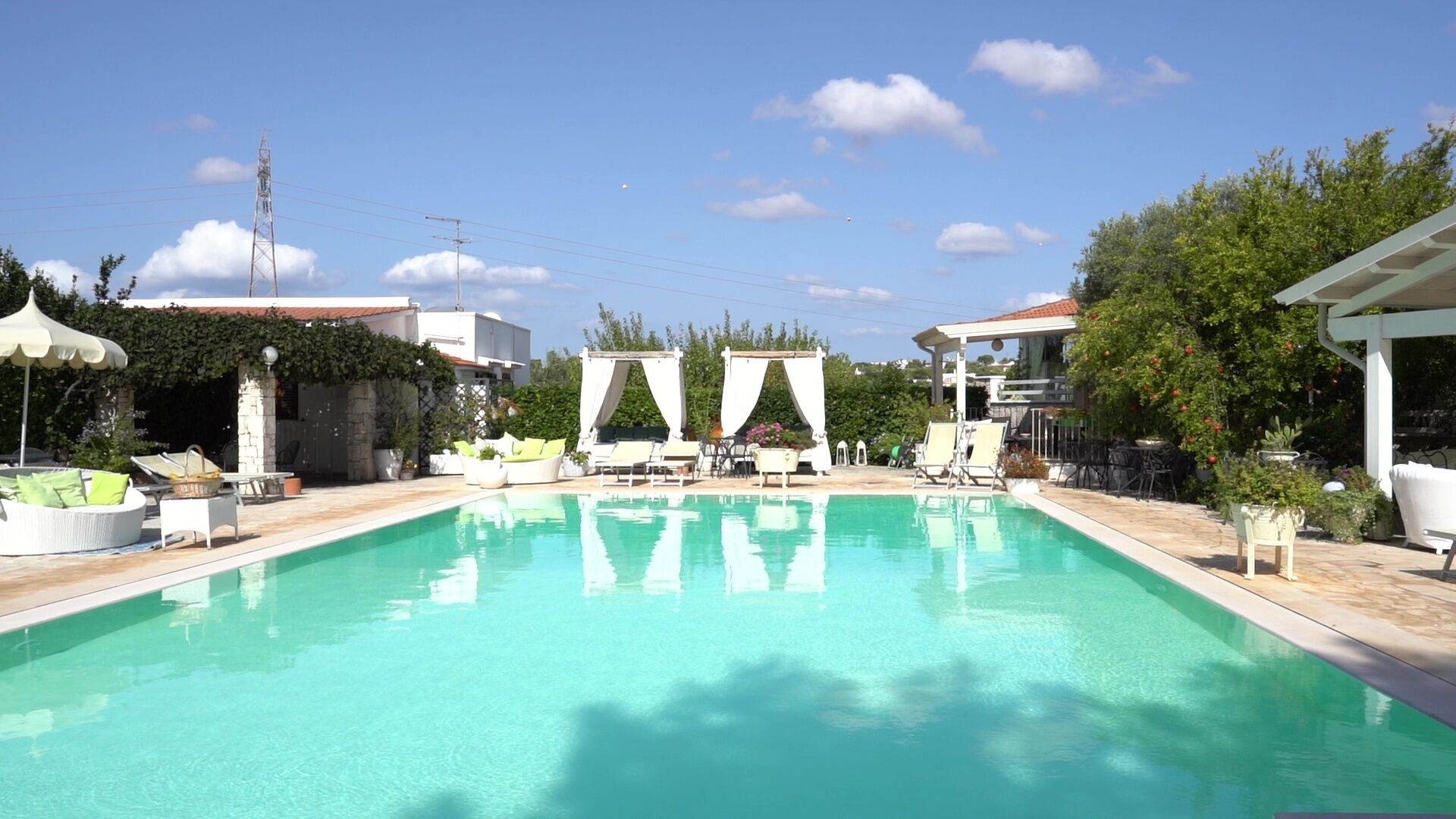 Una piscina con sillas de descanso y sombrillas, rodeada de vegetación y edificios.