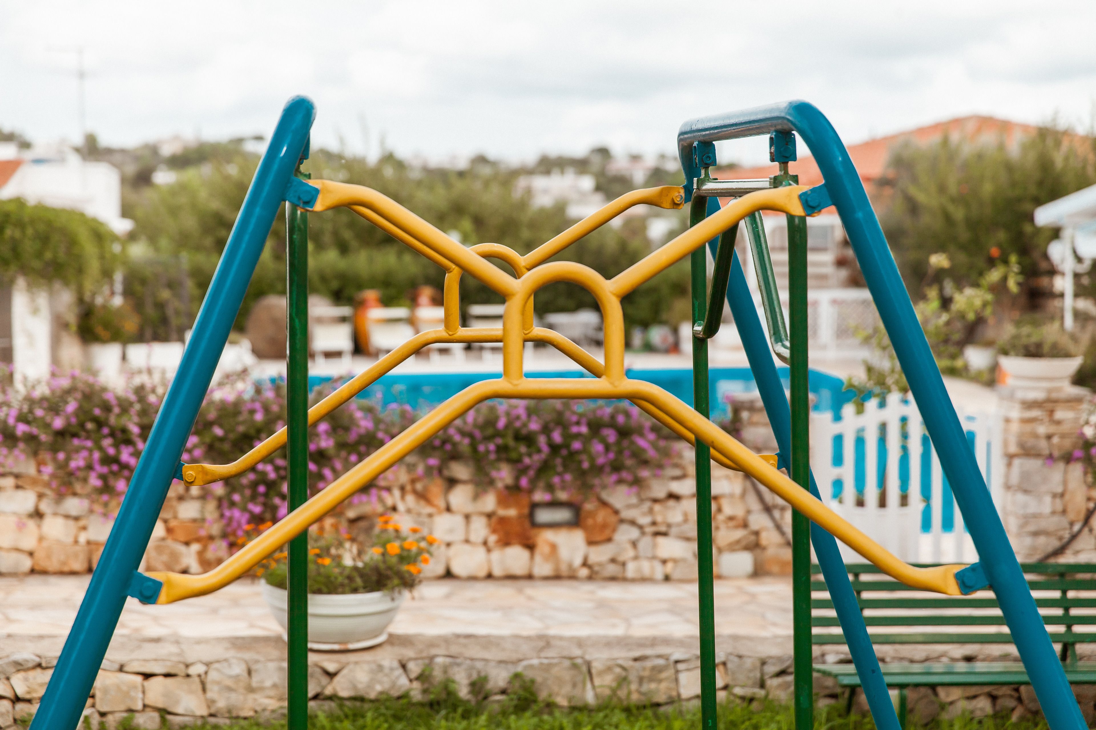 A playground with a yellow and blue climbing structure, surrounded by a stone wall and potted plants.