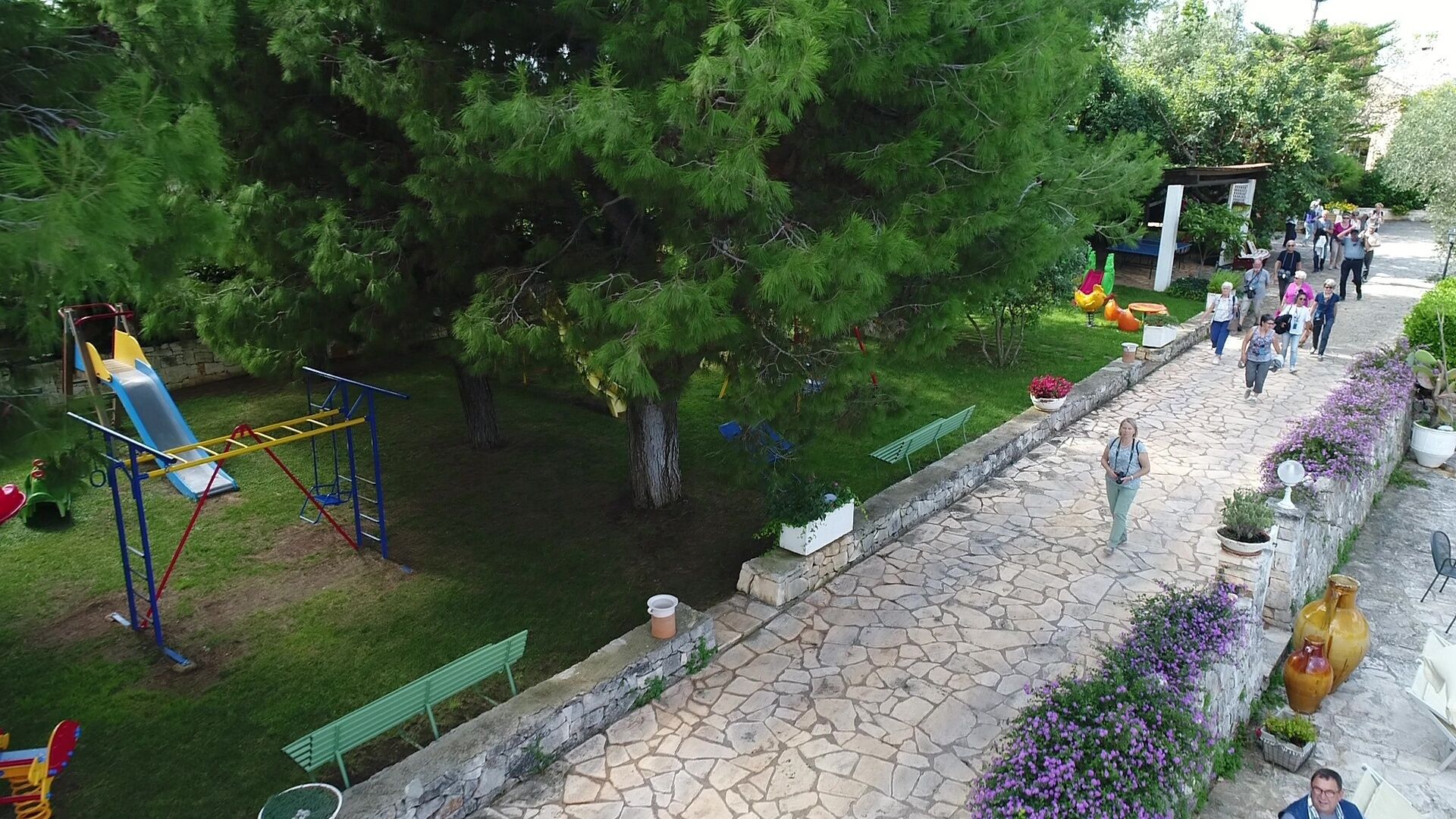 Un parque con un área de juegos, un camino de piedra y una fila de plantas en macetas.