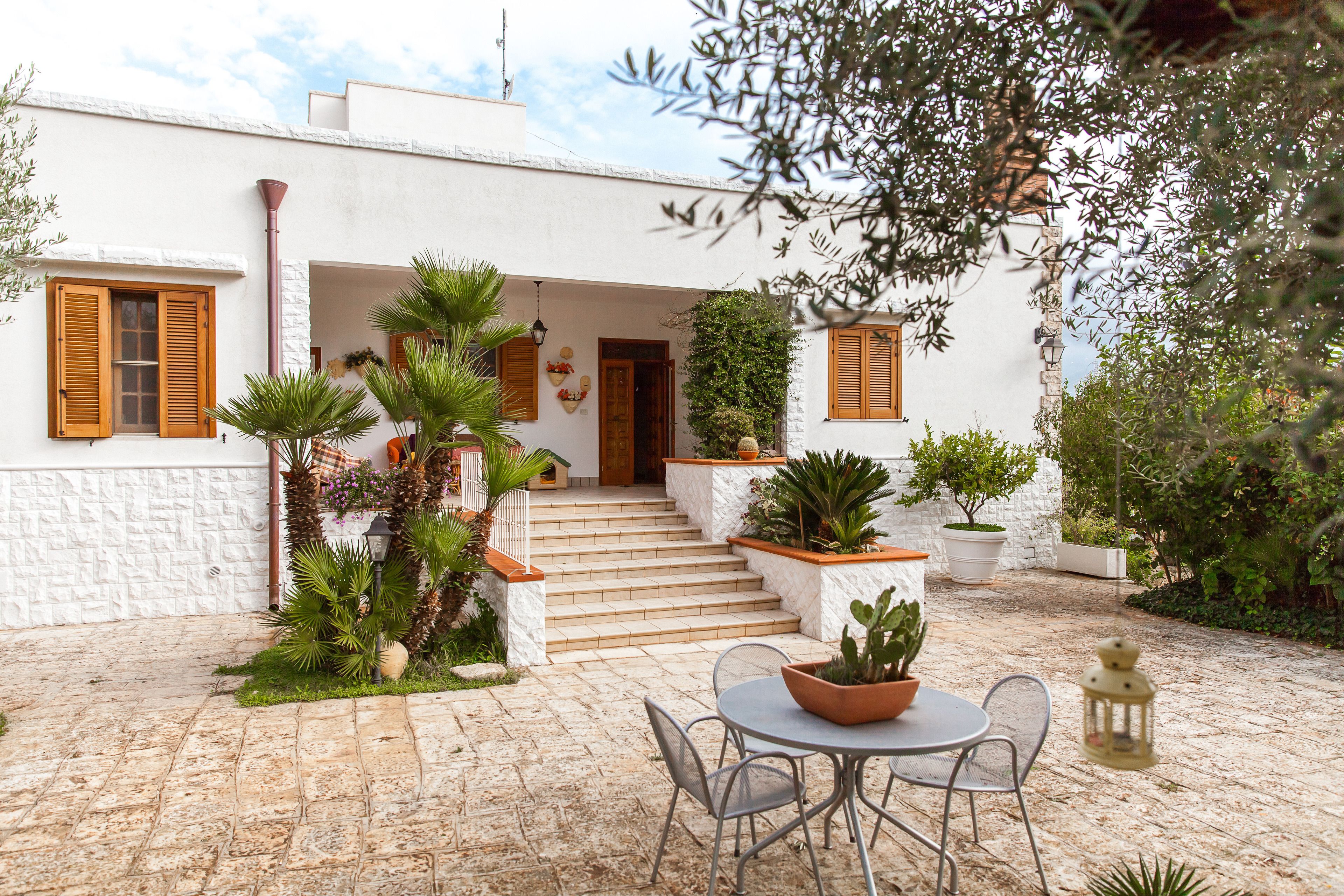 Un bâtiment blanc avec une façade en pierre, un escalier menant à une porte et un patio aménagé avec une table et des chaises.