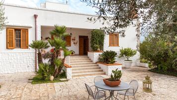 Un bâtiment blanc avec une façade en pierre, un escalier menant à une porte et un patio aménagé avec une table et des chaises.