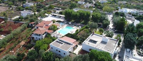 An aerial view of a residential area with houses, a swimming pool, and surrounding greenery.