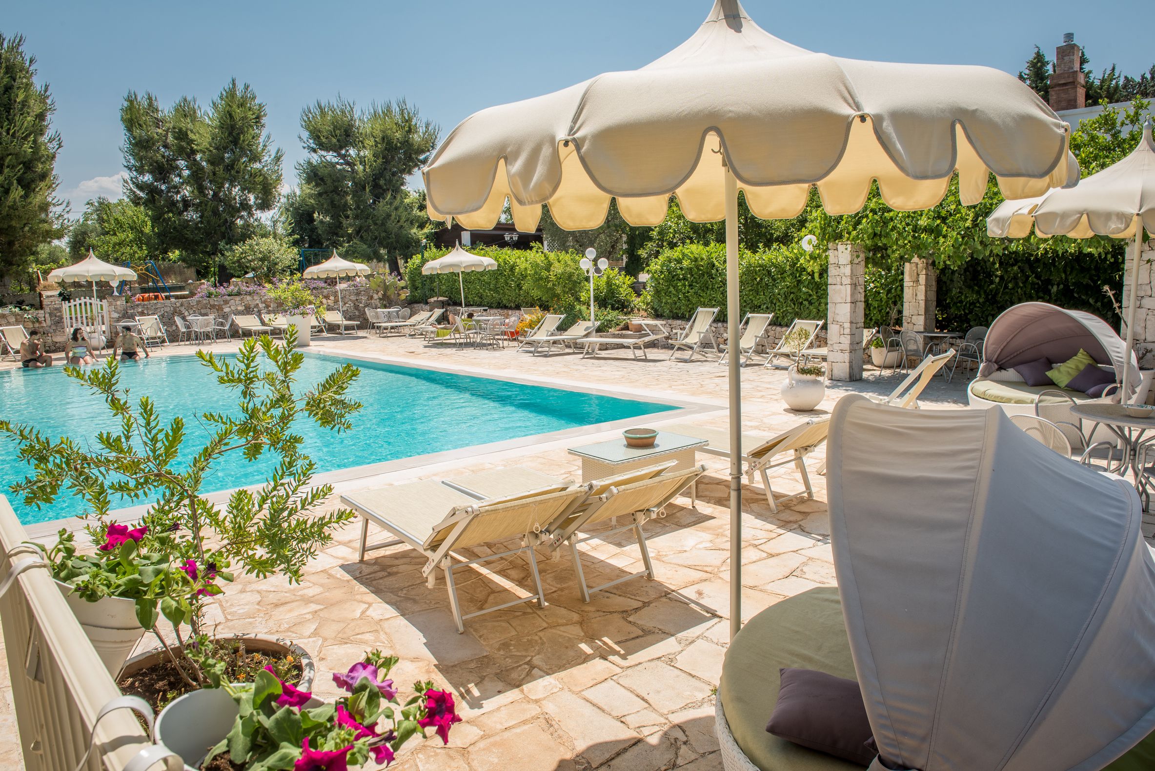 A poolside area with lounge chairs, umbrellas, and potted plants.