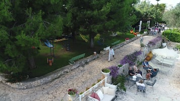 A stone-paved patio with outdoor seating, a playground, and a garden area with trees and flowers.