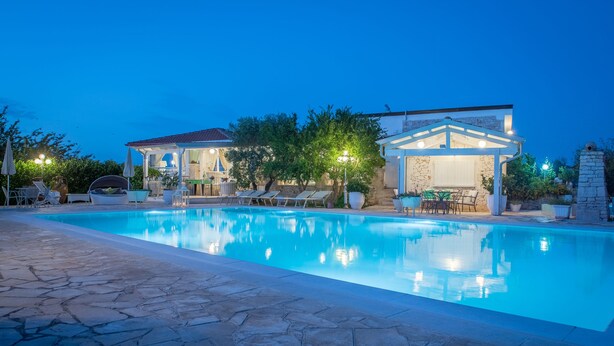 A swimming pool with lounge chairs and a gazebo, surrounded by stone walls and trees. - Agriturismo Salinola (Ostuni)