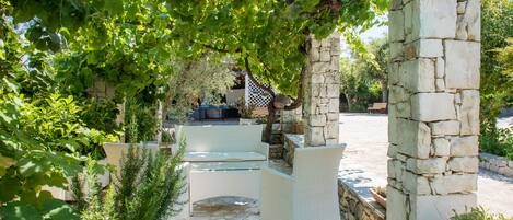 A stone pillar, a white wicker bench, and a stone pathway in a garden setting.