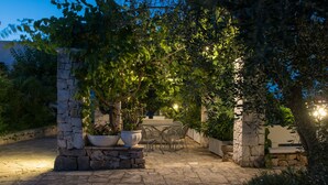 An outdoor patio with stone pillars, a table, and chairs, surrounded by greenery and stone walls. - Agriturismo Salinola (Ostuni)